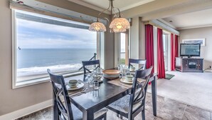 A dining area with a view of the ocean, a television, and a red curtain. - Condo #29 has AMAZING unsurpassed views of the Pacific Ocean! (Lincoln City)
