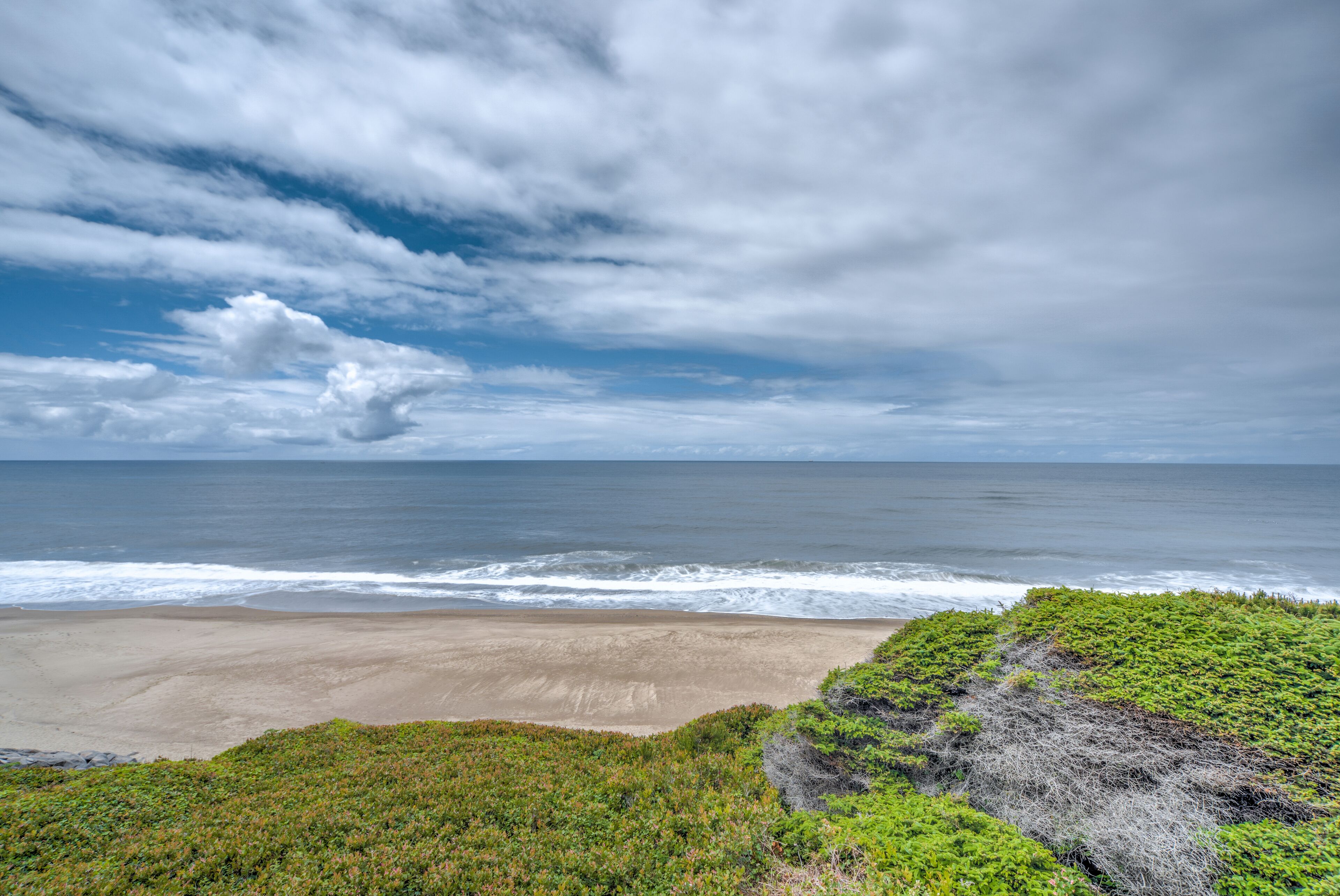 A beach with waves, a clear sky, and green vegetation.