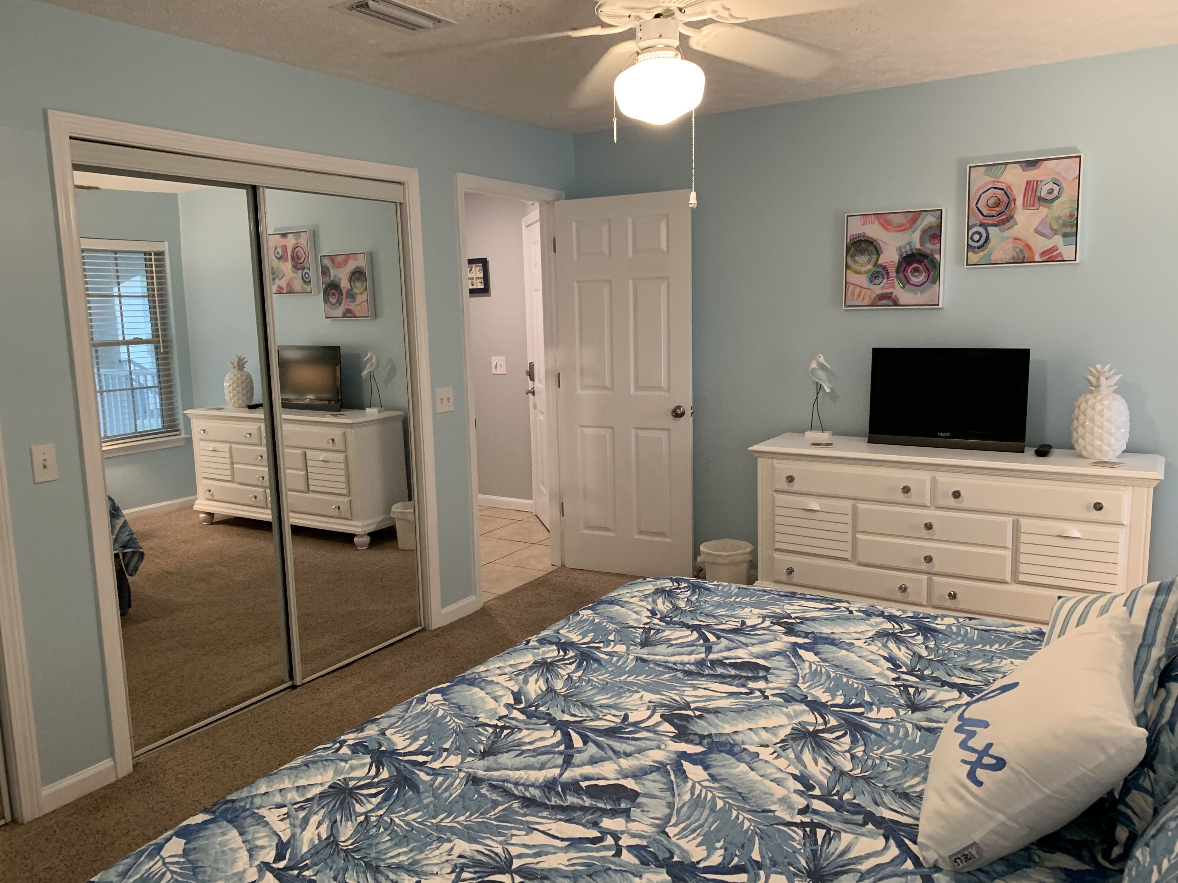 Un dormitorio con cama, cómoda, televisor y obras de arte en la pared.