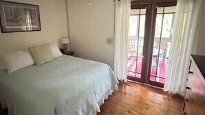 A bedroom with a bed, a ceiling fan, a nightstand, a dresser, and a door leading to an outdoor area. - Waterfront 2 Bd cabin on Blue River, PRIVATE RIVER ACCESS, kayaking, fishing (Corydon)
