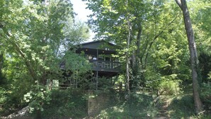 A rustic cabin with a balcony overlooking a river, surrounded by dense greenery. - Waterfront 2 Bd cabin on Blue River, PRIVATE RIVER ACCESS, kayaking, fishing (Corydon)