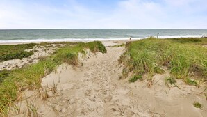 A sandy beach path leading to the ocean with grassy dunes on either side.