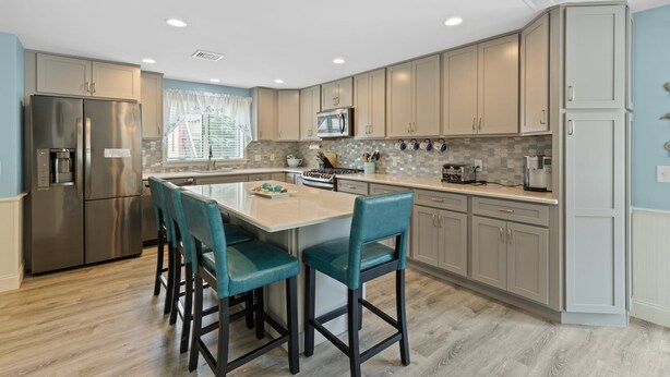 A modern kitchen with a central island, stainless steel appliances, and teal bar stools.