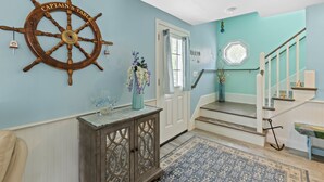 A nautical-themed entryway with a ship's wheel, a wooden console, a staircase, and a patterned rug.