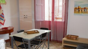 A compact dining area with a table, chairs, a bench, a refrigerator, and a patterned floor. - TRAPANI HOLIDAY HOME LOW COST 2 (TRAPANI)