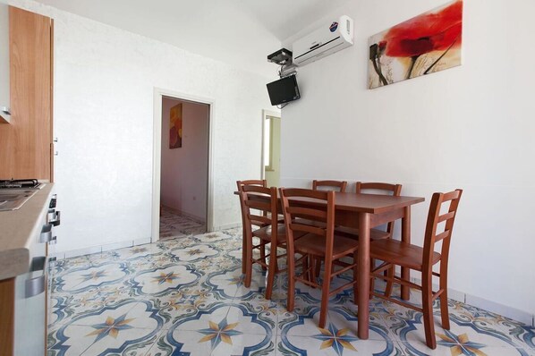 A dining area with a wooden table and chairs, a tiled floor, and a kitchen with a stove.