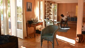 A spacious living area with a sofa, a wicker chair, a dining table, and a person working at a desk. - House / Villa - AUPS (Aups)