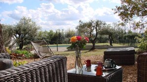 A patio area with wicker furniture, a table with a vase of flowers, and a view of a pool and trees. - House / Villa - AUPS (Aups)