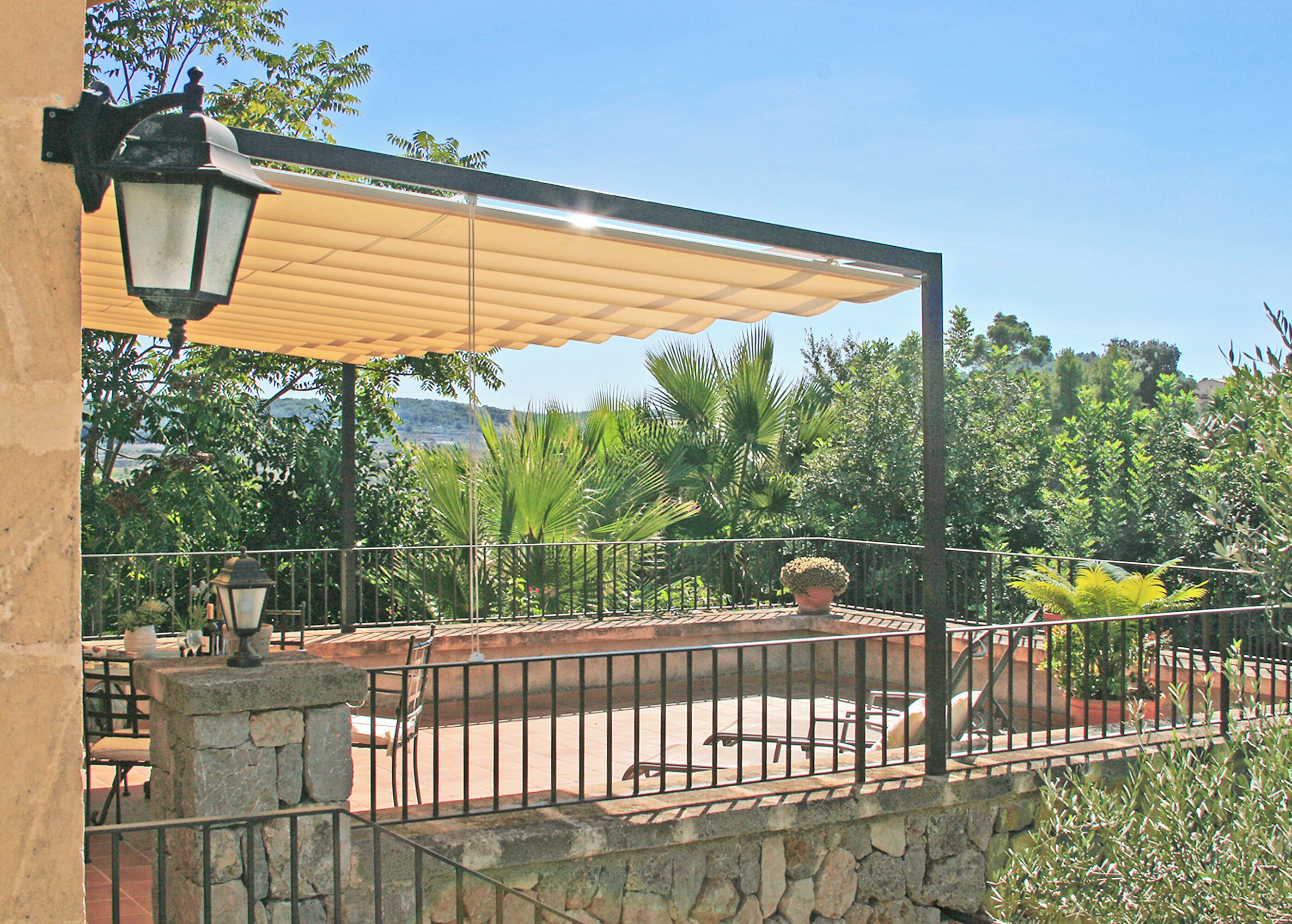 A patio area with a stone wall, metal railing, and a canopy providing shade.