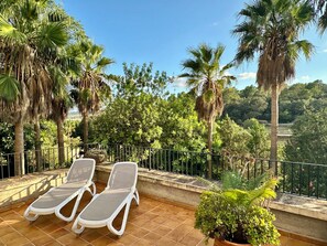 Een terras met twee witte lounge fauteuils, een bloempot en uitzicht op palmbomen en groen.