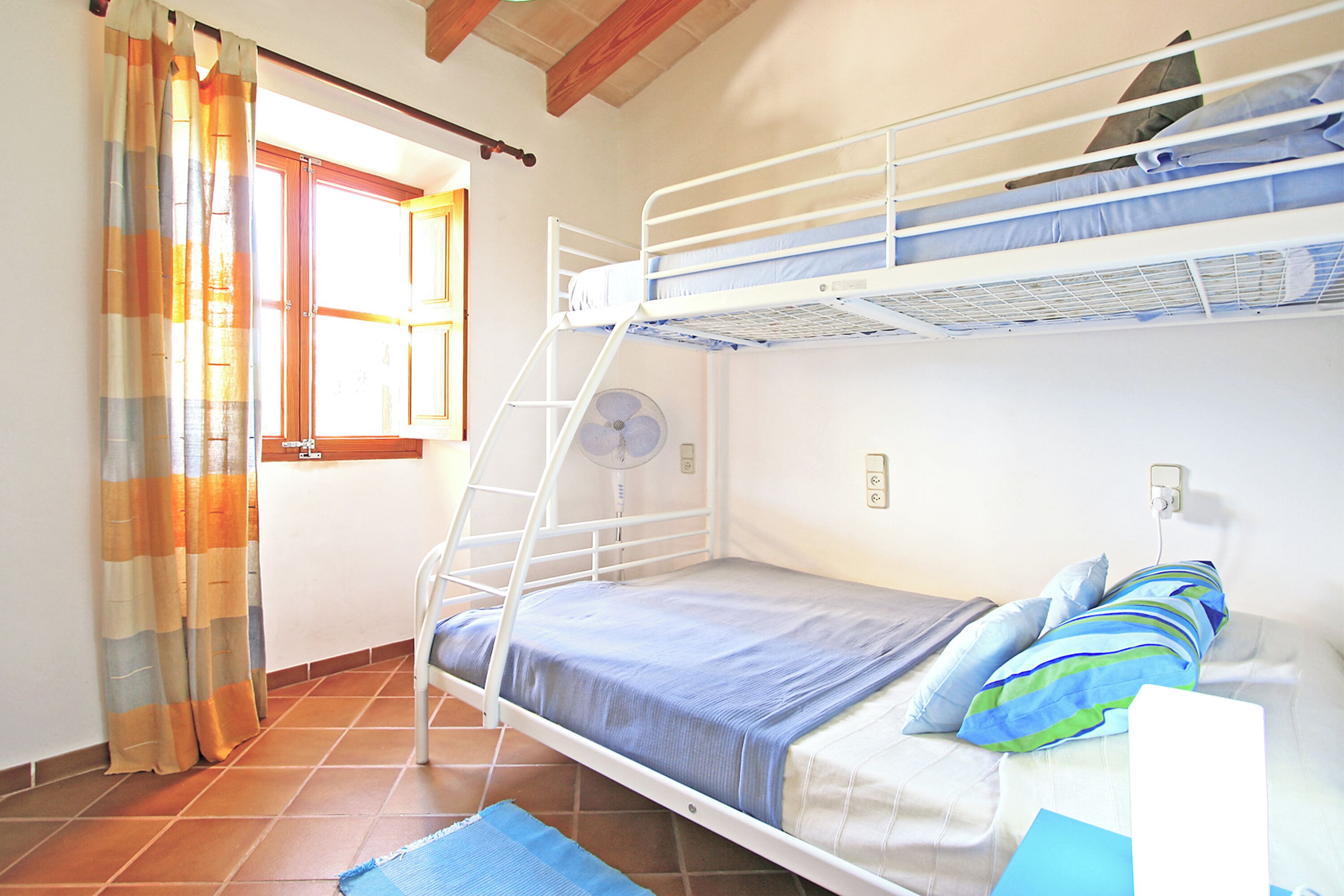 A bunk bed room with a window, curtains, and a fan.