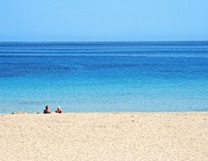 Een strand met twee personen zittend in het zand, uitkijkend over de oceaan.