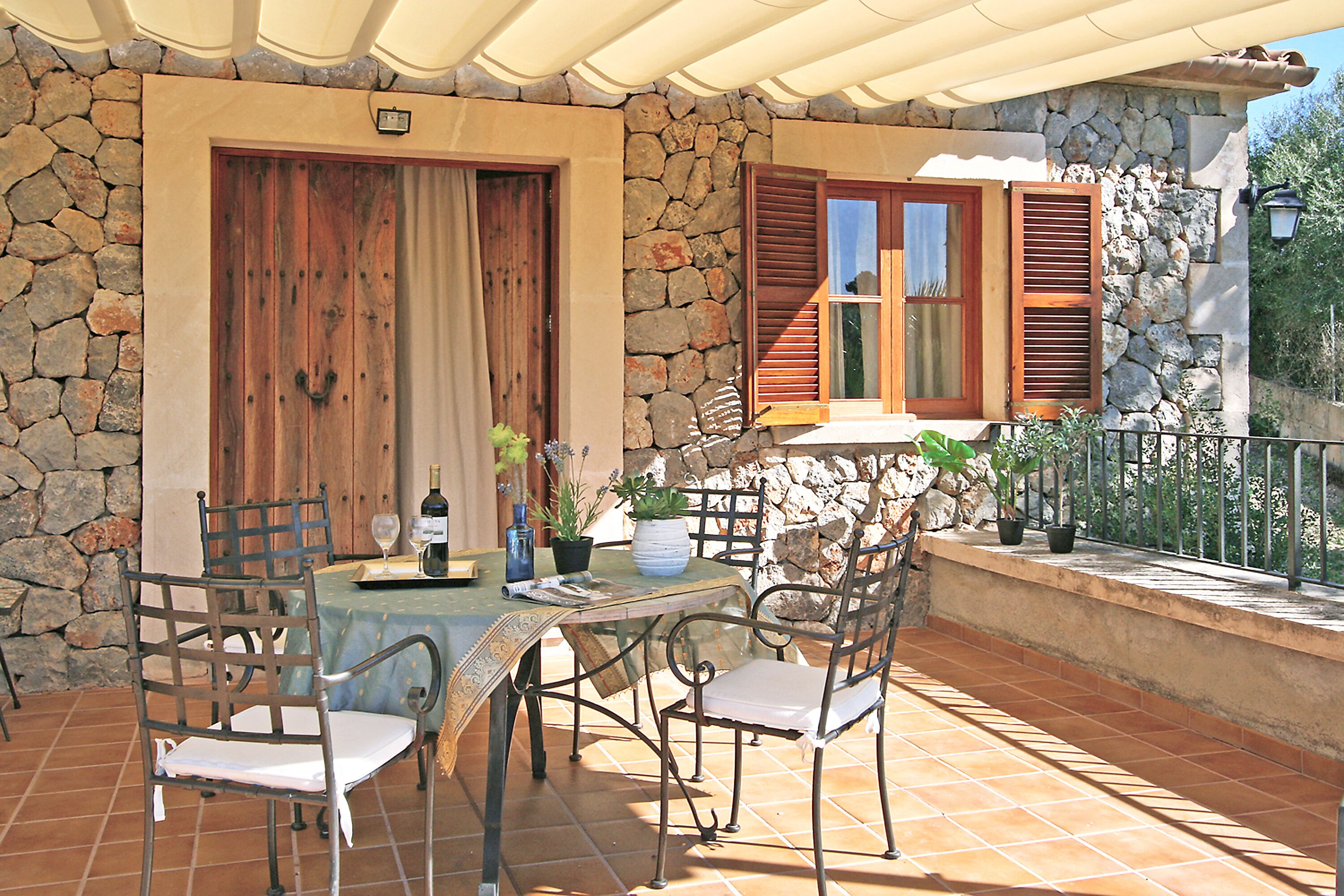 A stone-walled outdoor patio with a table and chairs, a wooden door, and a window with shutters.