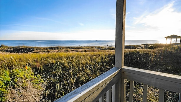 A wooden deck overlooking a beach with a gazebo in the distance.