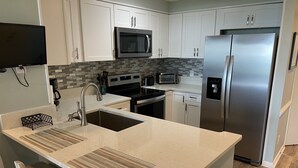 A modern kitchen with white cabinets, a stainless steel refrigerator, a microwave, an oven, and a dishwasher.