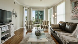 A living room with a television, two armchairs, a sofa, a coffee table with plants, and a view of a balcony with a railing. - GORGEOUS BEACH VIEW Legacy Towers T1-Unit 308/3 pools/Hot Tub/Close to Casinos (Gulfport)
