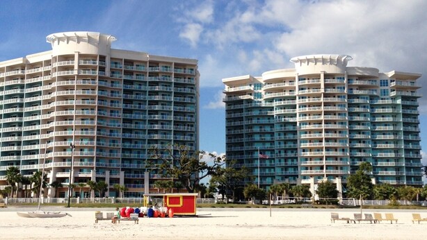 A beachfront hotel with multiple floors, balconies, and a beachside area with lounge chairs and a small red building. - GORGEOUS BEACH VIEW Legacy Towers T1-Unit 308/3 pools/Hot Tub/Close to Casinos (Gulfport)