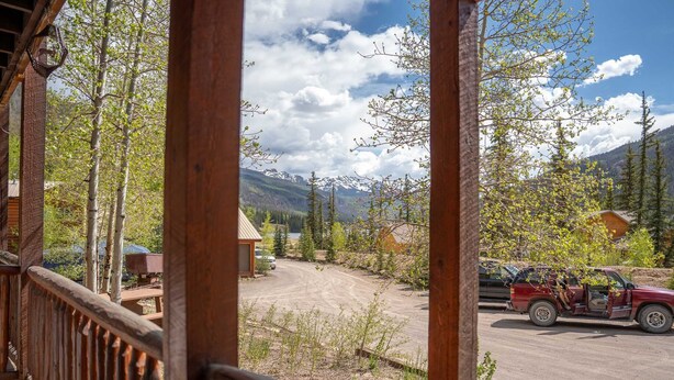 Una terraza de madera con vistas a un paisaje montañoso, un camino de tierra y un vehículo estacionado.