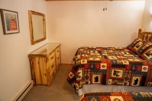 A bedroom with a wooden dresser, a bed with a quilt, a mirror, and a framed picture on the wall.
