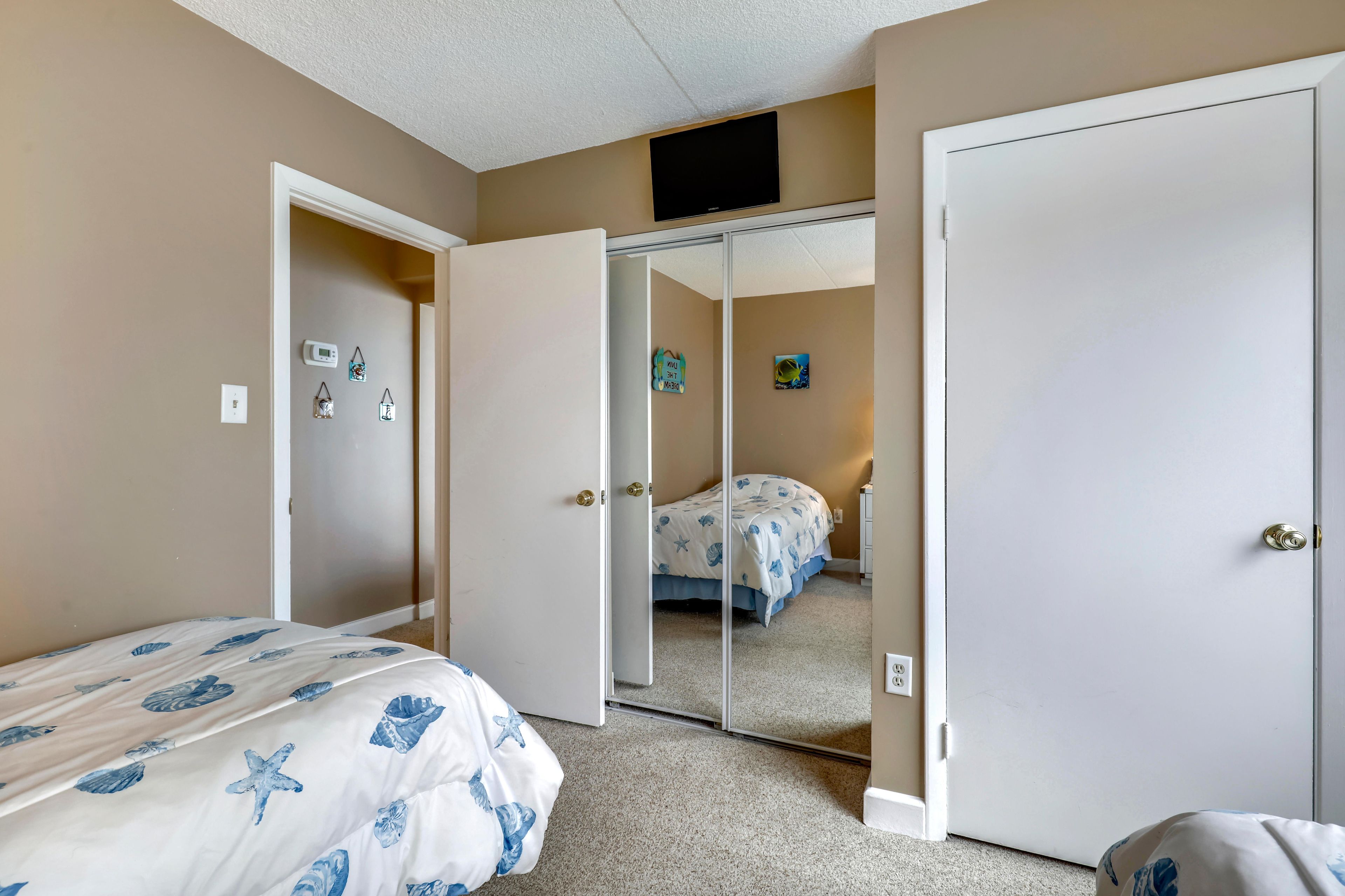 Une chambre à coucher comprenant un lit, une armoire, un miroir et un thermostat fixé au mur.