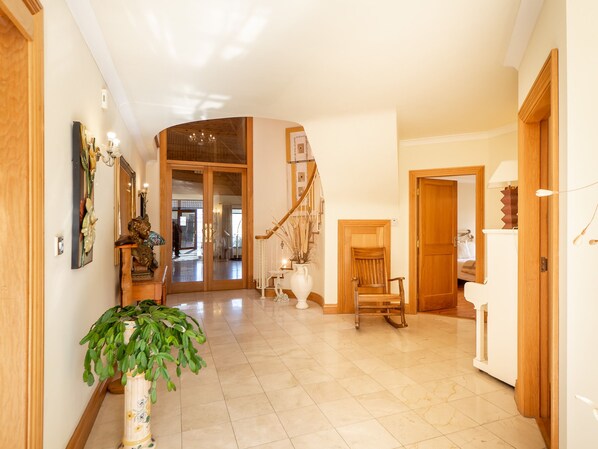 A spacious hallway with a wooden staircase, a potted plant, and a chair. - Spectacular Setting Overlooking Beach (Cleggan)
