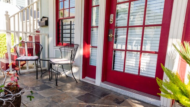A red door with a mailbox, a metal chair, and a potted plant on a stone patio. - Classic & Central Hollywood Retreat with Porch and Garden (Los Angeles)