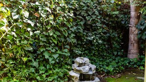 A garden with a stone fountain surrounded by dense green foliage. - Classic & Central Hollywood Retreat with Porch and Garden (Los Angeles)