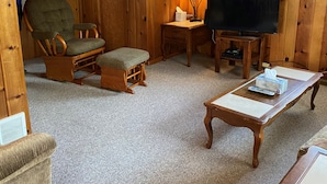 A cozy cabin interior with wooden walls, a television, a lamp, and a chair. - Beautiful Year-Round  Home on the South Shore of Hubbard Lake (Spruce)