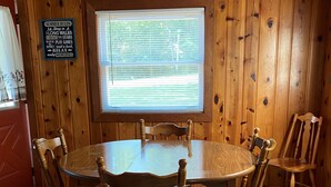 A wooden-paneled room with a round table and six chairs. A sign on the wall lists summer activities. - Beautiful Year-Round  Home on the South Shore of Hubbard Lake (Spruce)