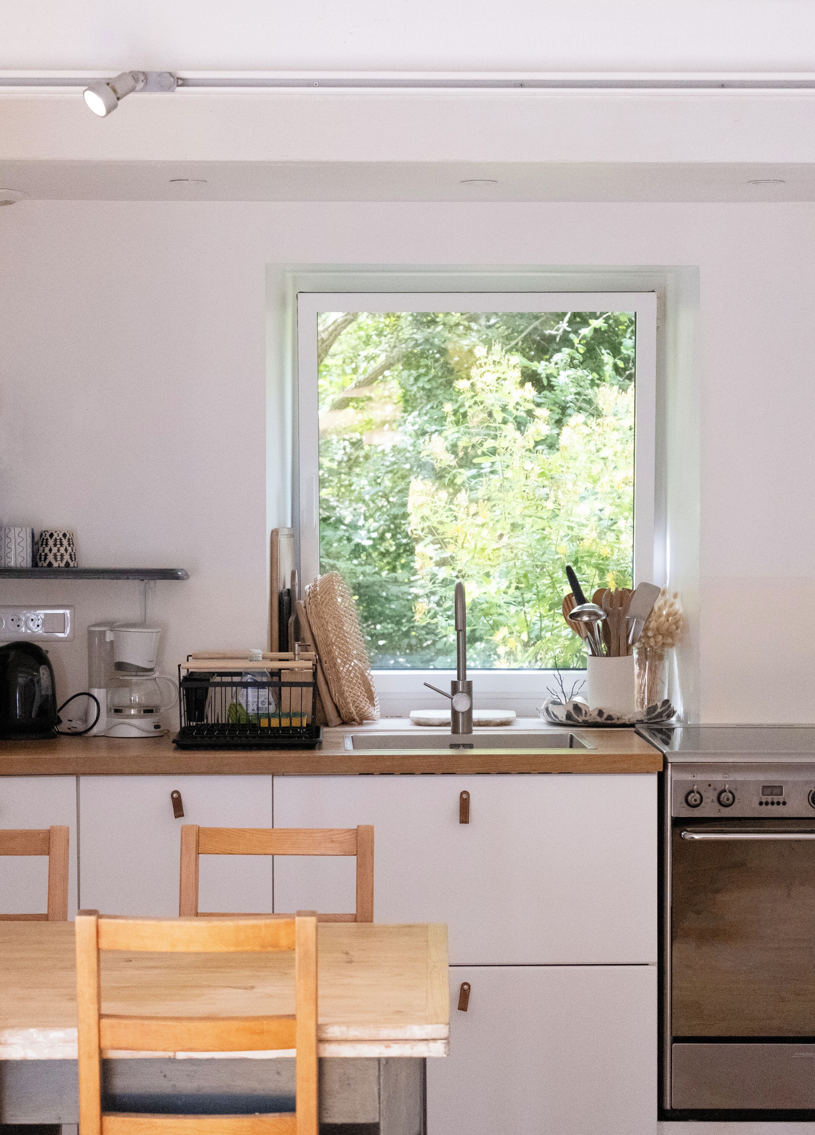 Une cuisine avec une fenêtre, un évier, une cuisinière et un coin repas avec des chaises.