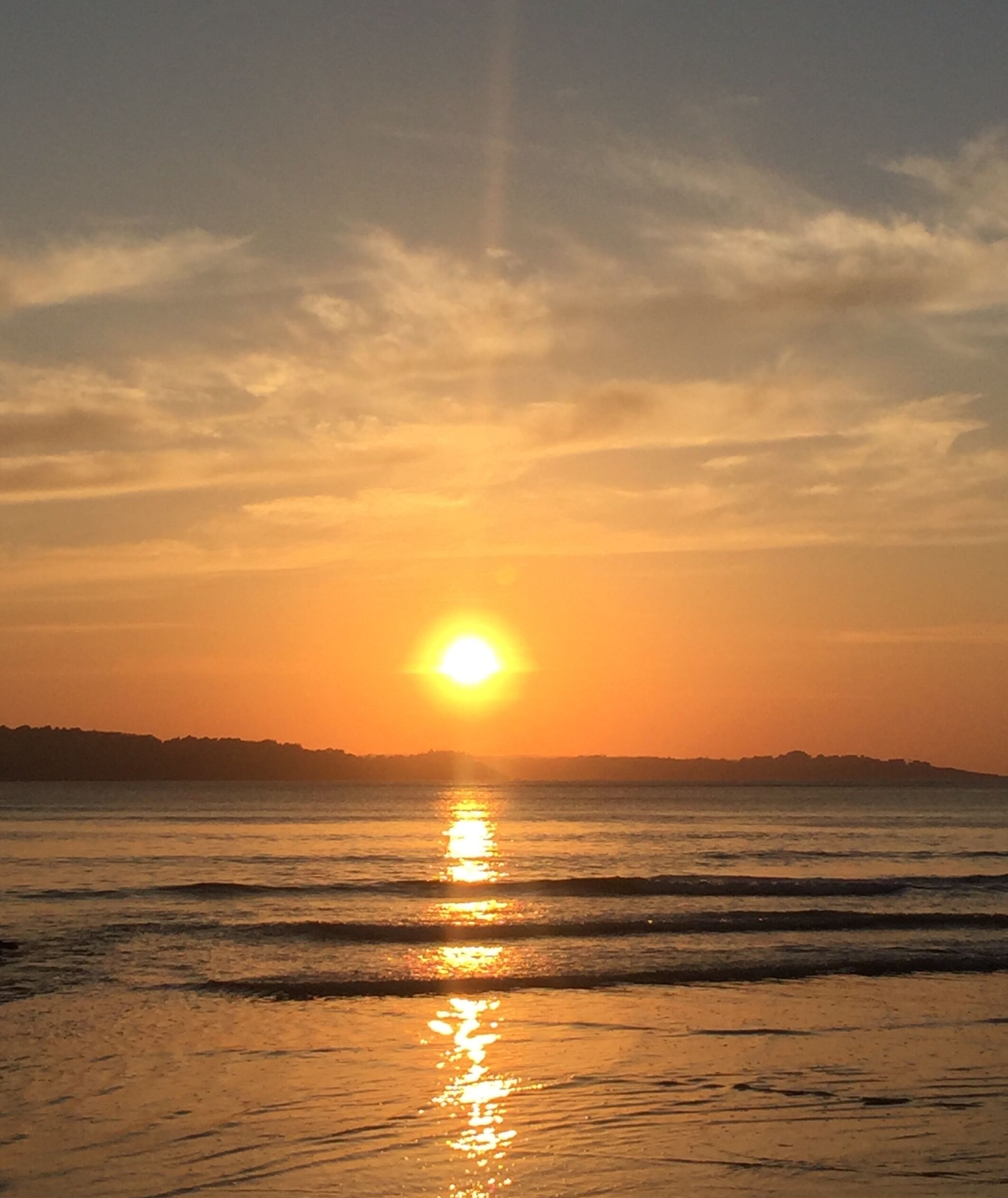 Un coucher de soleil sur une plage, le soleil se reflétant sur l’eau.