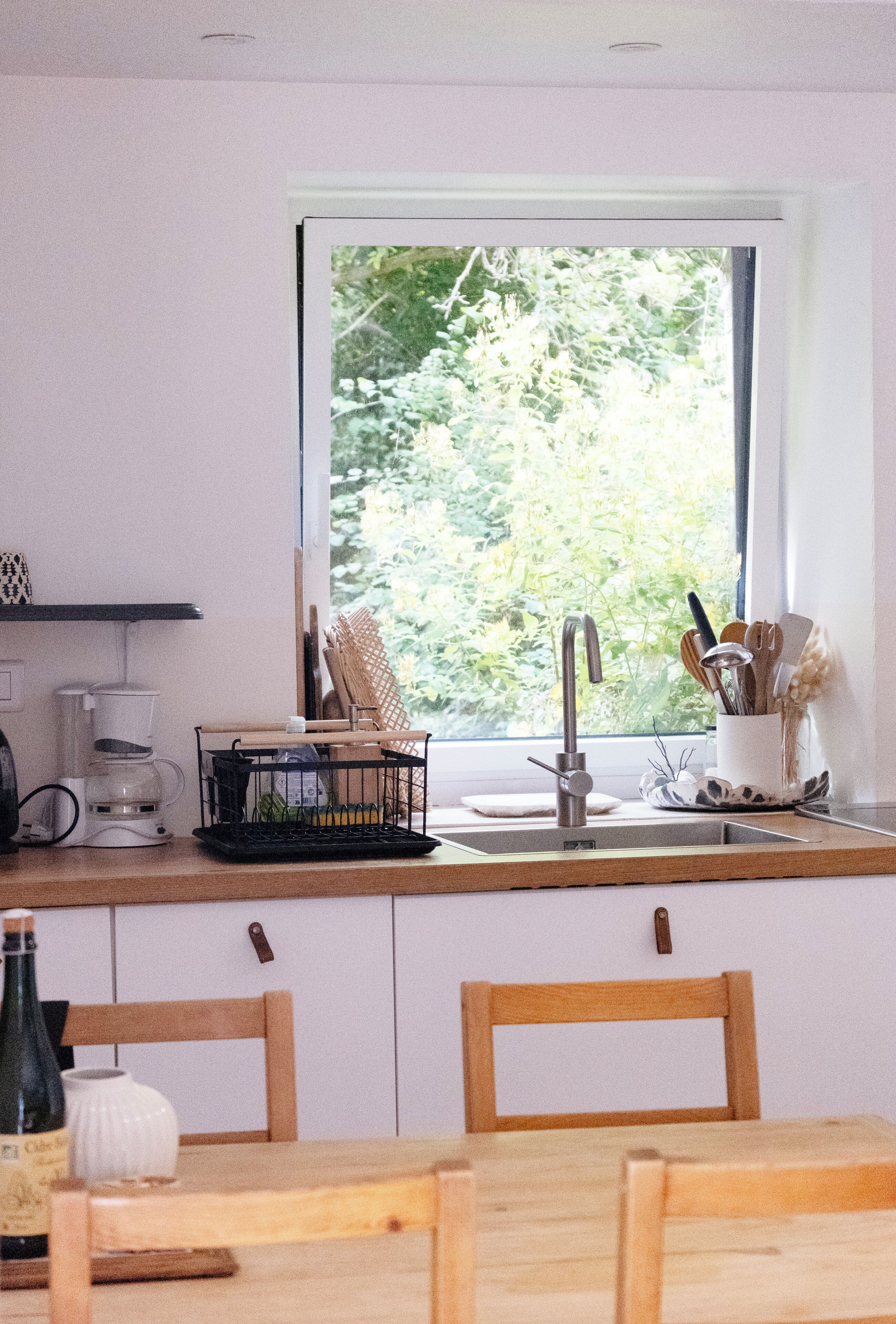 A kitchen with a window, a coffee maker, a sink, and a dining area with chairs.