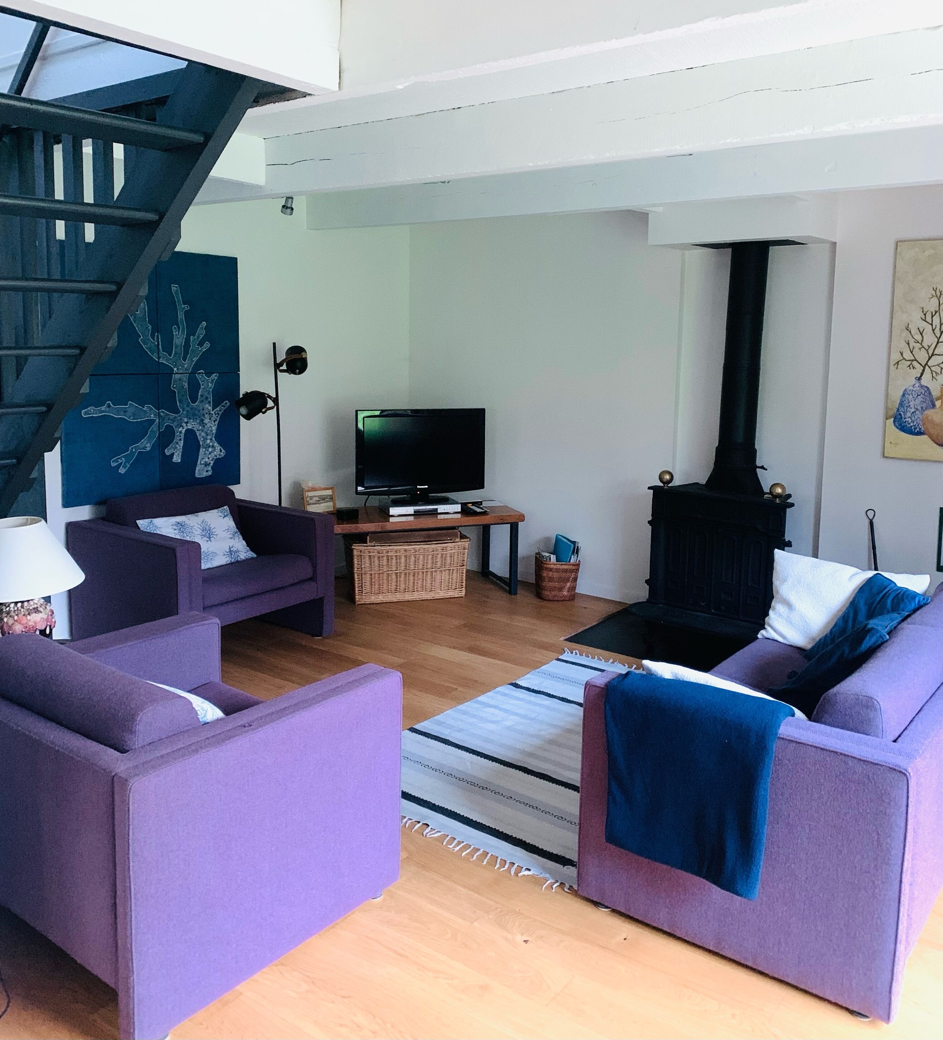 Un salon avec un escalier, un téléviseur, une cheminée et des canapés violets.