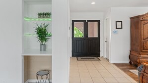 A hallway with a black door, a wooden cabinet, and a shelf with plants.