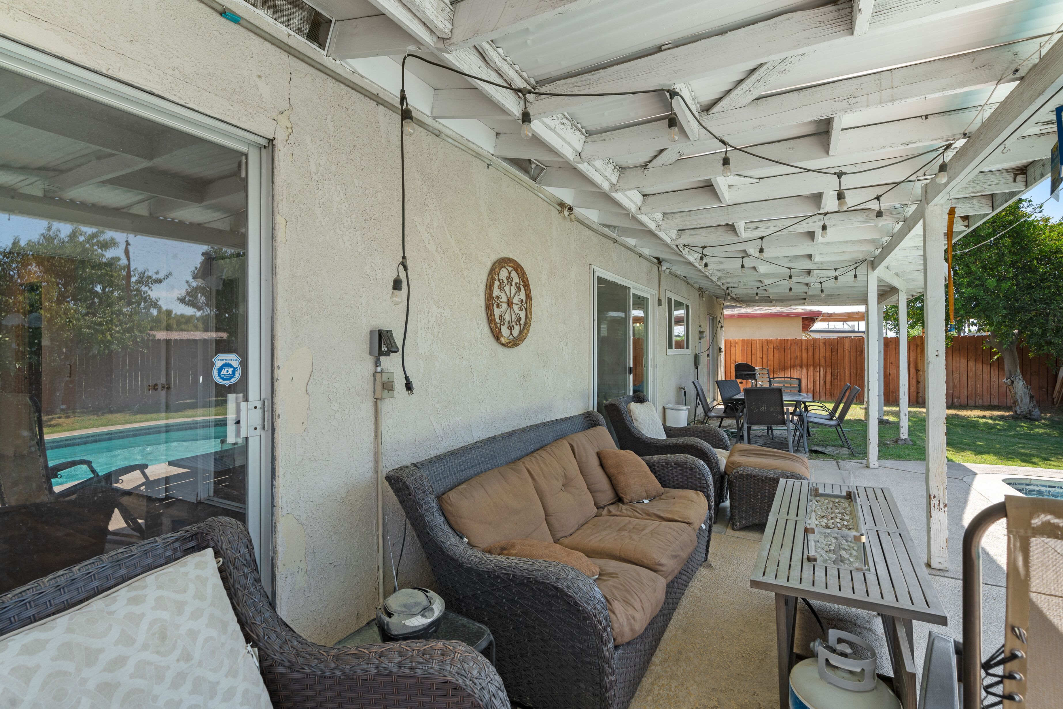 A covered patio area with wicker furniture, a table, and a view of a swimming pool.