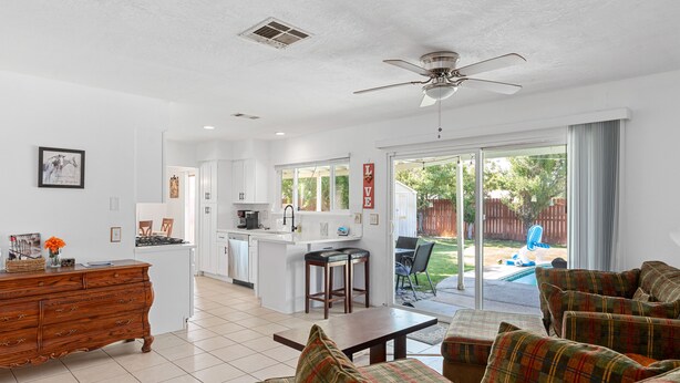 A spacious living room with a plaid sofa, a wooden coffee table, and a kitchen area with white cabinets and a central island.