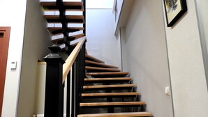 Un escalier en colimaçon avec des marches en bois et des rampes noires, menant à un palier équipé d’un radiateur et d’une petite table.
