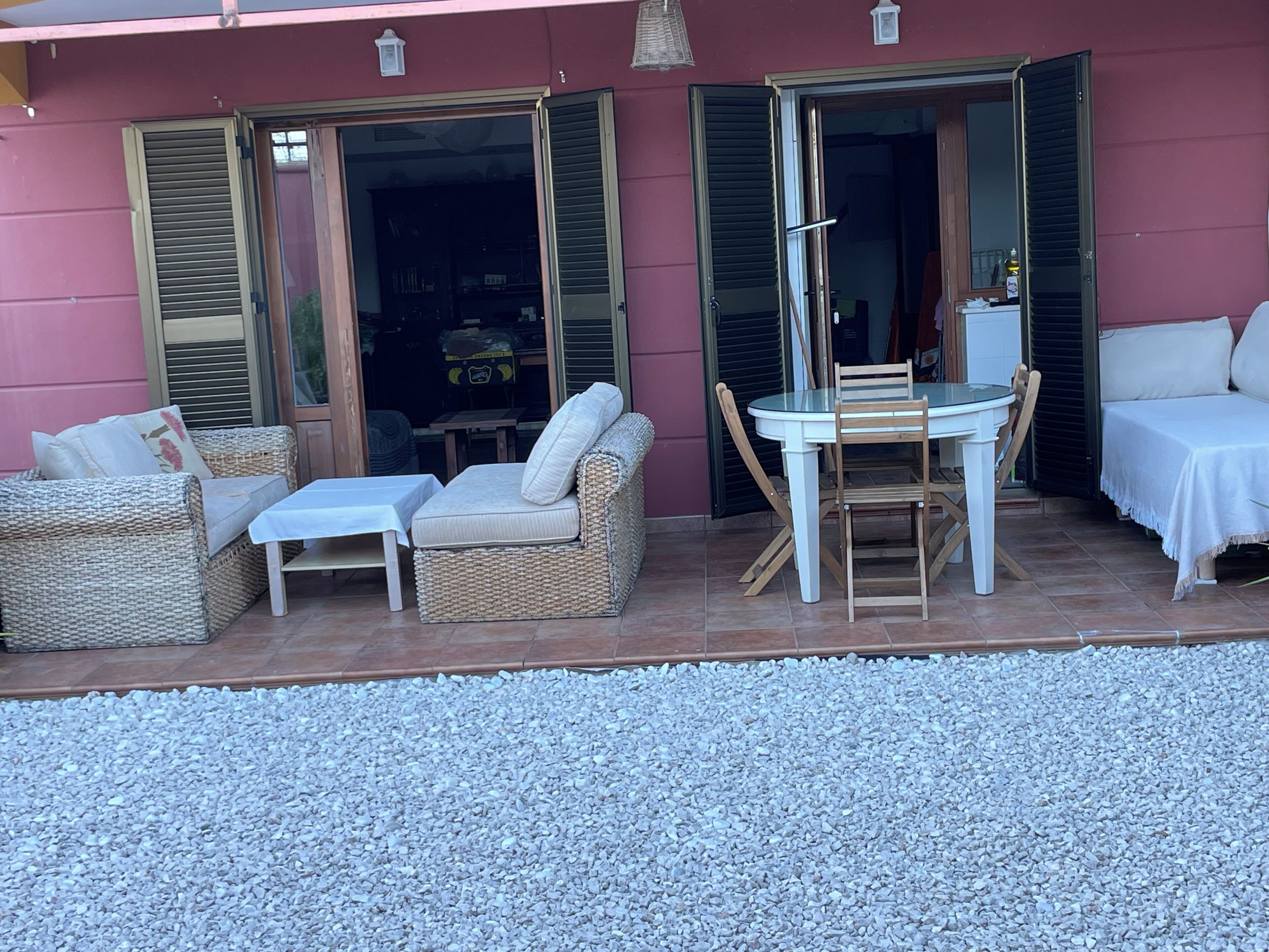 An outdoor patio with wicker furniture, a glass table, and a white sofa.
