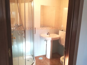 Et badeværelse med brusekabine i glas, et håndvaskarrangement og et toilet.