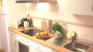 A kitchen with a dishwasher, a sink, a stove, and a countertop with fruits and a bottle.
