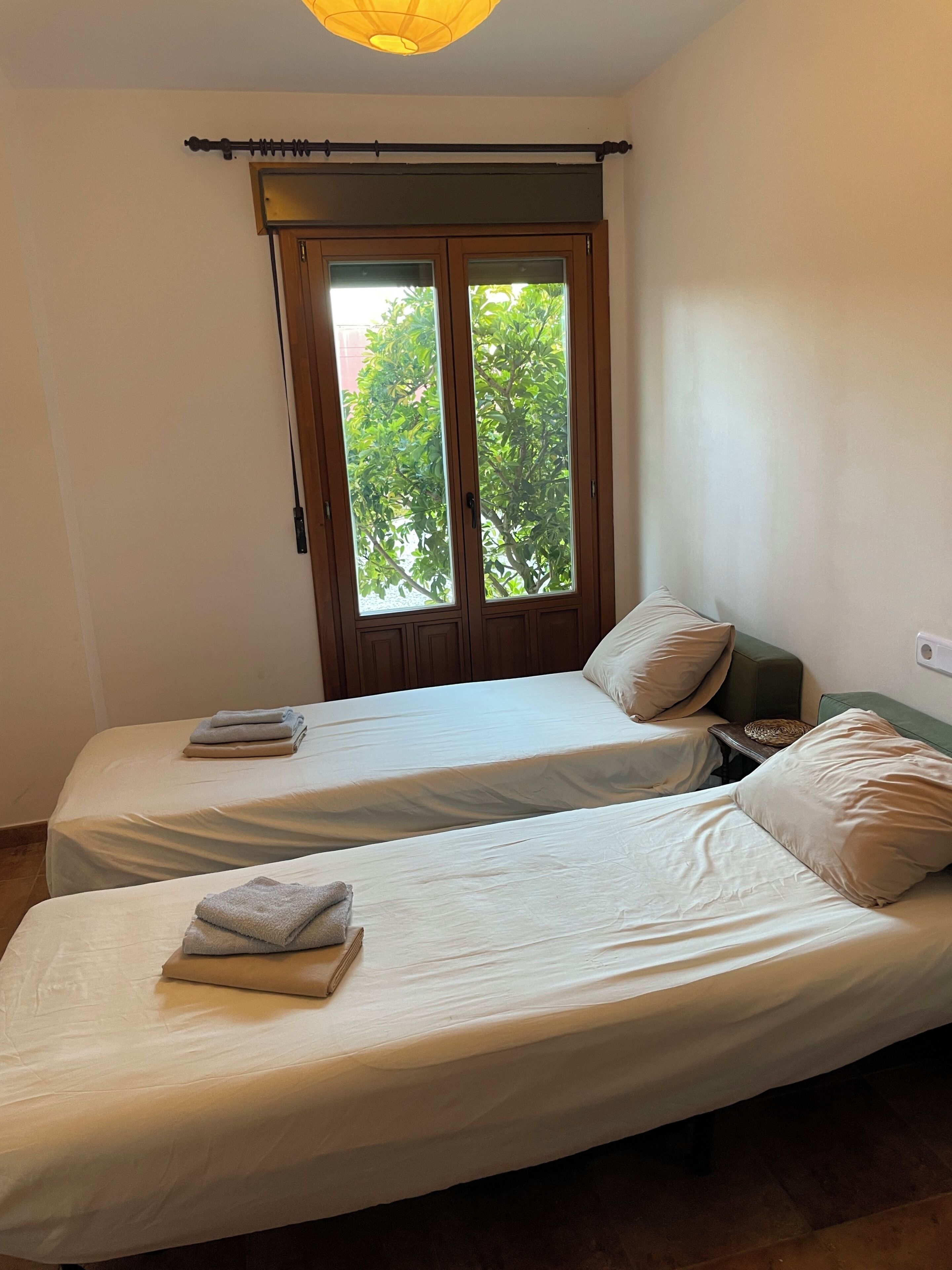 Een kamer met twee bedden, een raam met uitzicht op groen en een plafondlamp.