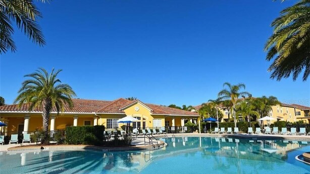 Un resort con una gran piscina, palmeras y edificios amarillos con techos de tejas rojas.