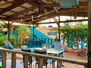 Une terrasse extérieure avec des meubles en bois, un hamac et une vue sur un immeuble à la façade bleue et jaune.