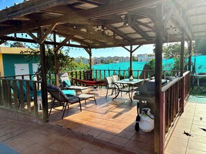 Une terrasse extérieure couverte, agrémentée d’une pergola en bois, d’un sol carrelé et de mobilier d’extérieur comprenant des chaises et une table.
