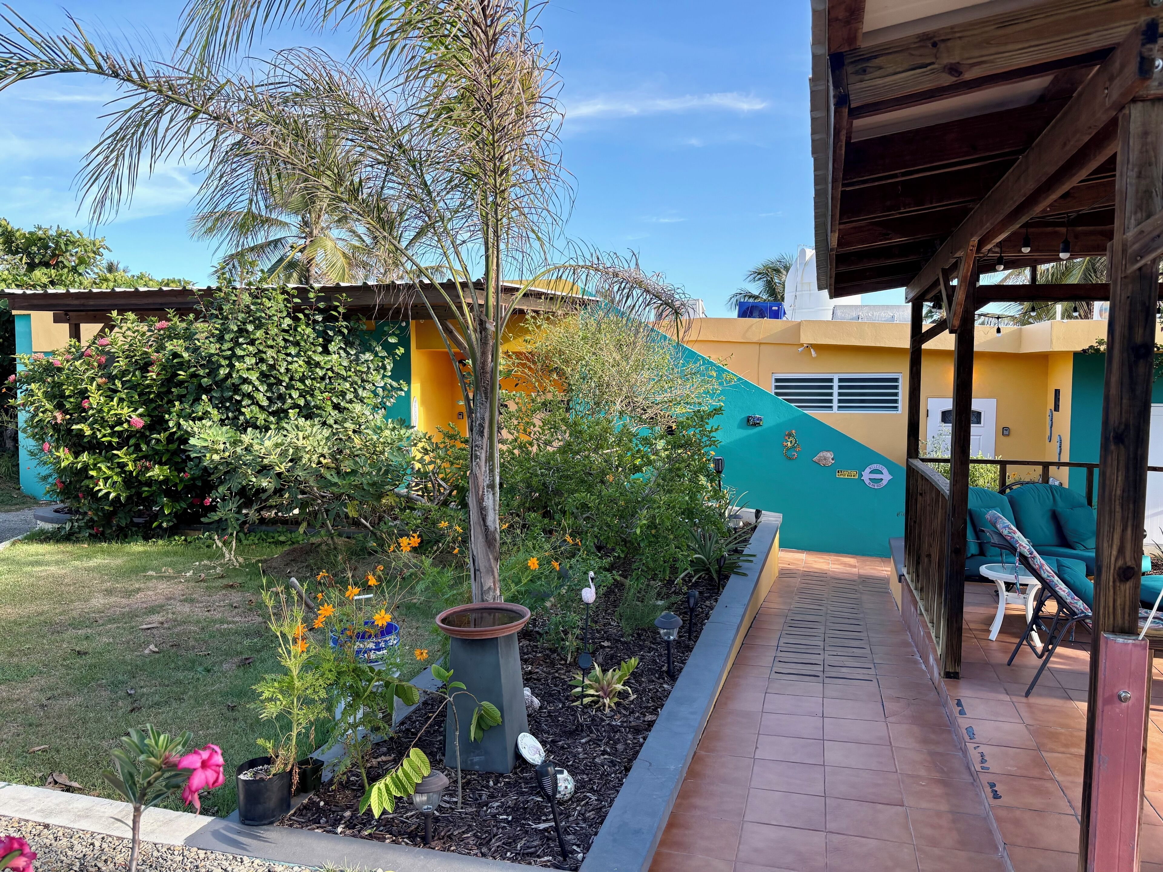 A patio area with a wooden pergola, outdoor seating, and a variety of plants and flowers.
