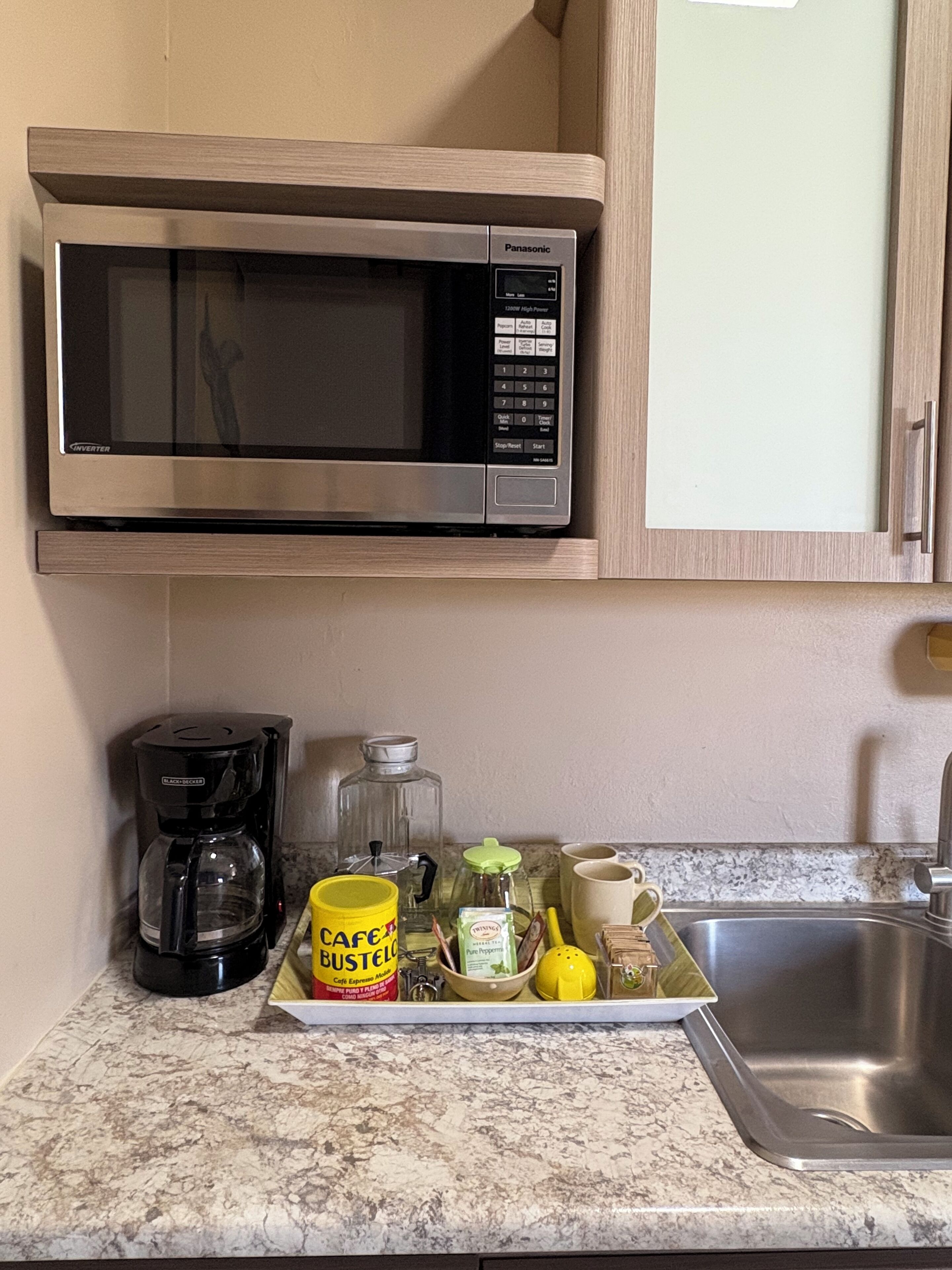 A kitchen with a built-in microwave, a coffee maker, a glass carafe, a yellow mug, and a sink.