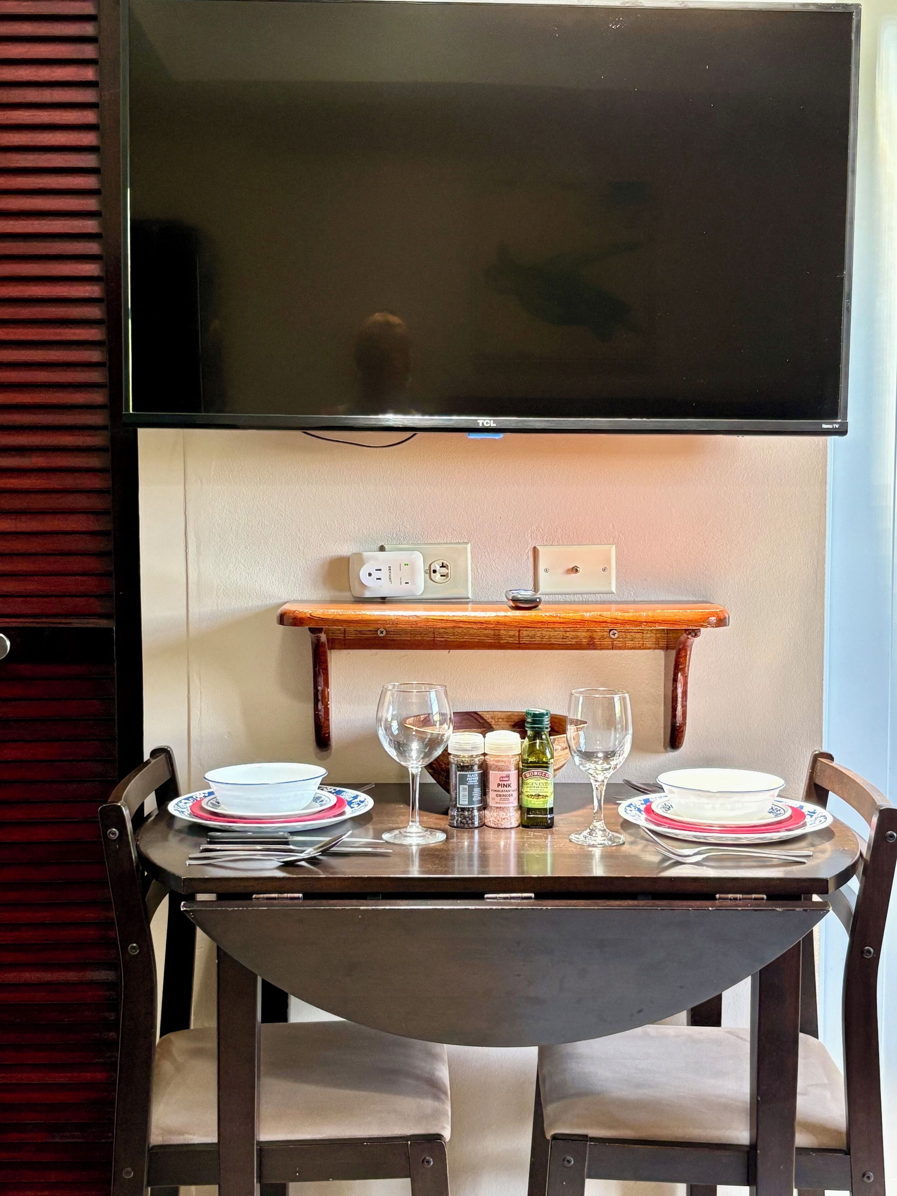 A dining table with chairs, a television above, and a shelf with items.