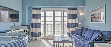 Una habitación con una cama a cuadros, un sofá y una mesa. Hay un televisor en la pared y un cuadro también.