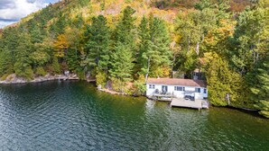 Une cabane au bord d’un lac, entourée d’arbres aux feuilles d’automne.
