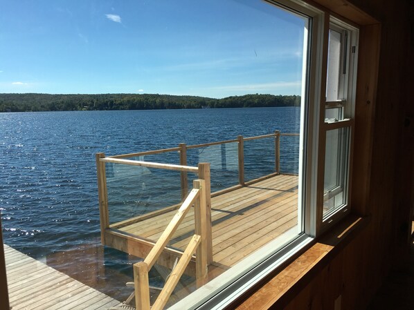 Una terraza de madera con barandilla de vidrio que da a un lago.